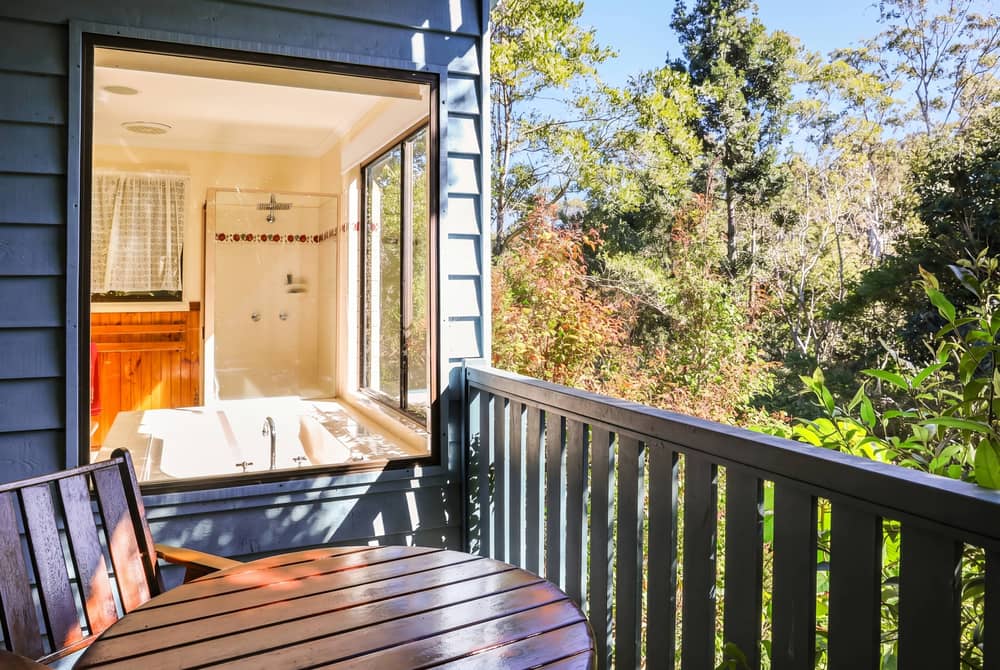 Spa bath on a cabin deck with glass doors opening to bushland beyond the railing