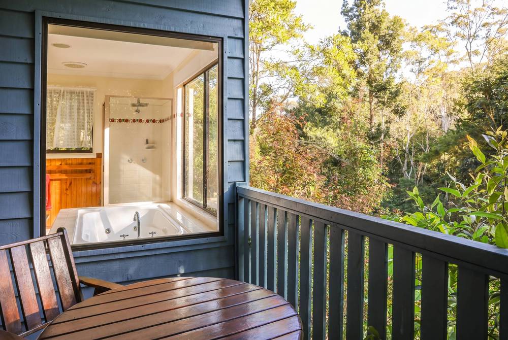 Spa bath window opening onto deck railing with bushland backdrop