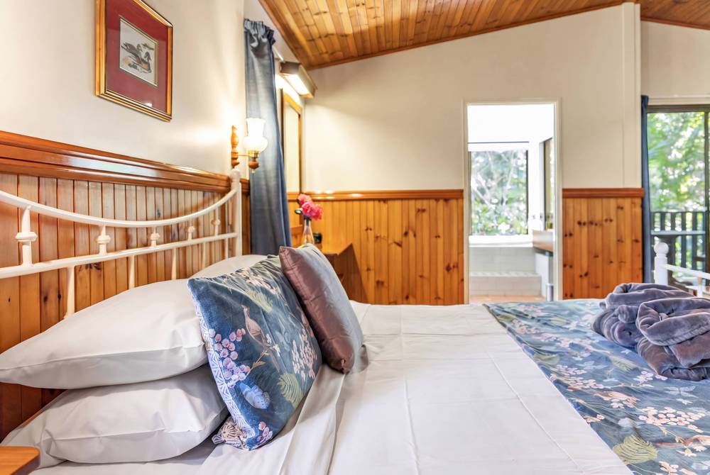 Timber bedroom with metal bed, wardrobes and windows showing outdoor trees