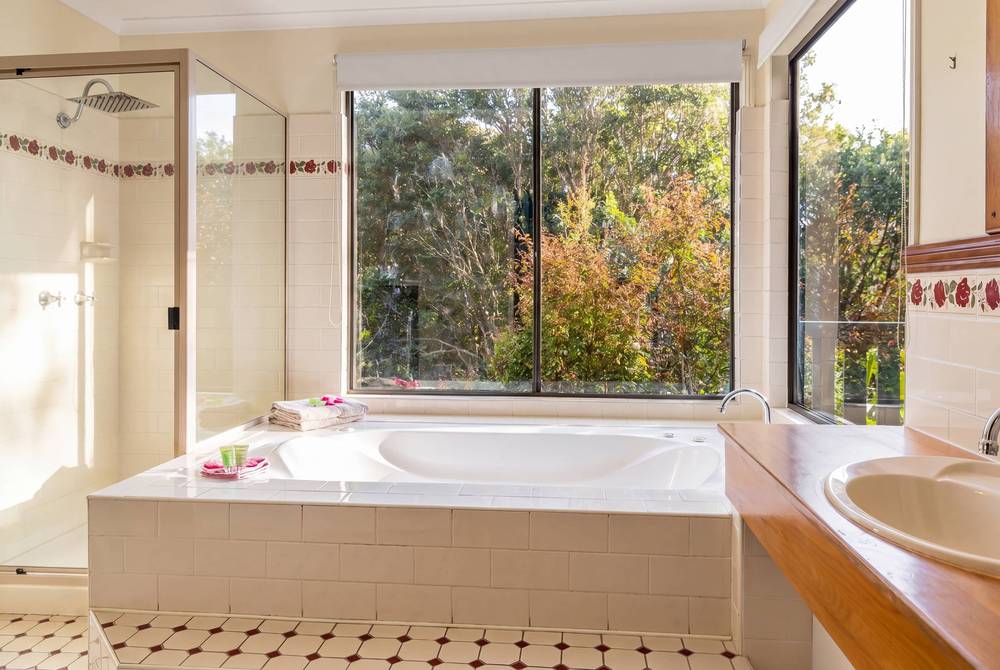 Spa bath beside rainforest-view window in tile bathroom