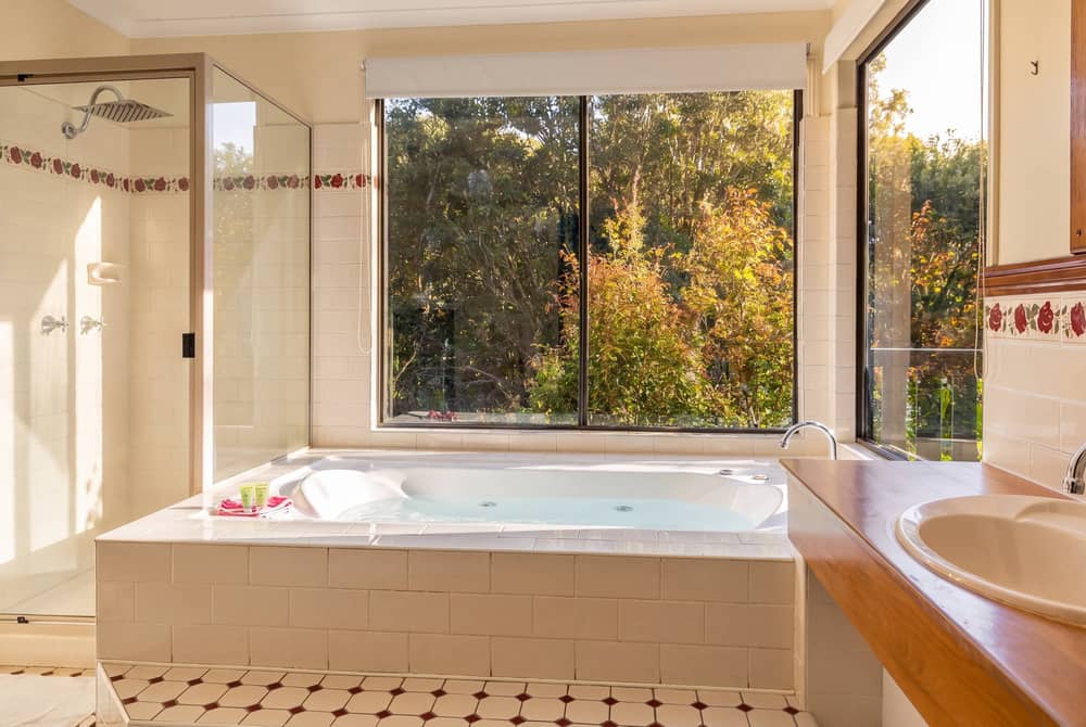 Spa bath beside rainforest-view windows with natural light