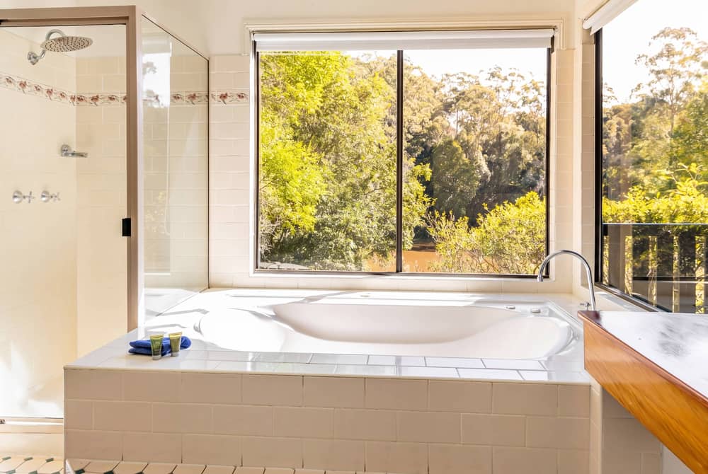 King-size spa bath with wide windows looking out over dense rainforest