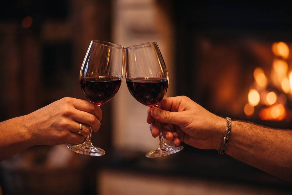 A couple toasting wine glasses in front of the fireplace