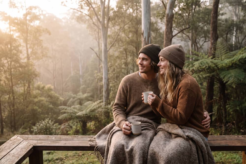 Couple with coffee cups on a timber bench overlooking the forested hinterland