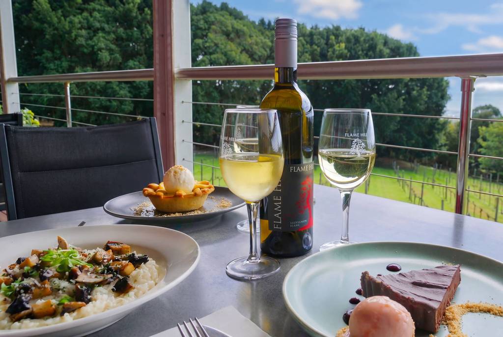 A deck restaurant table with wine and dishes above the vineyard