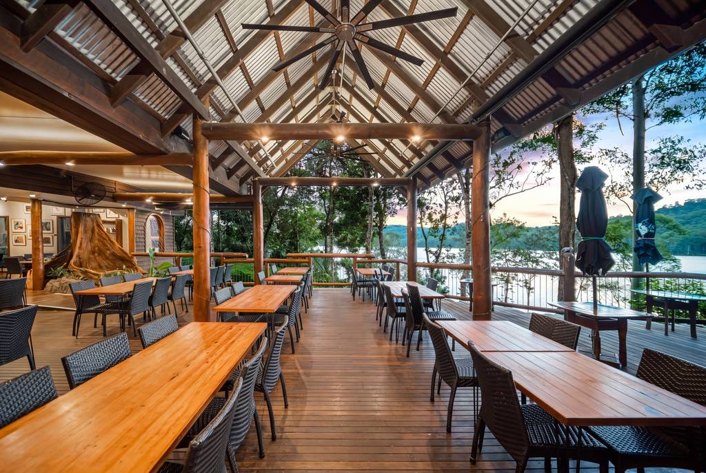 A timber deck restaurant with tables and a lake view framed by timber beams