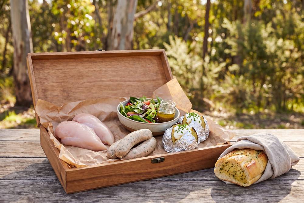 Timber hamper with raw chicken, salad and herb bread on wooden table