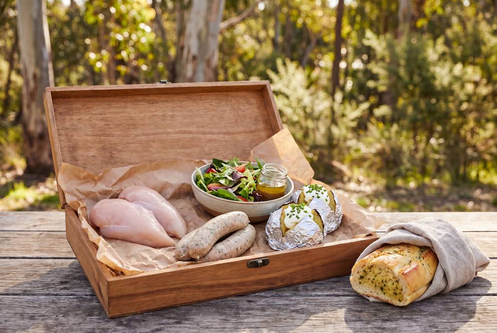 Timber hamper with raw chicken, salad and herb bread on wooden table
