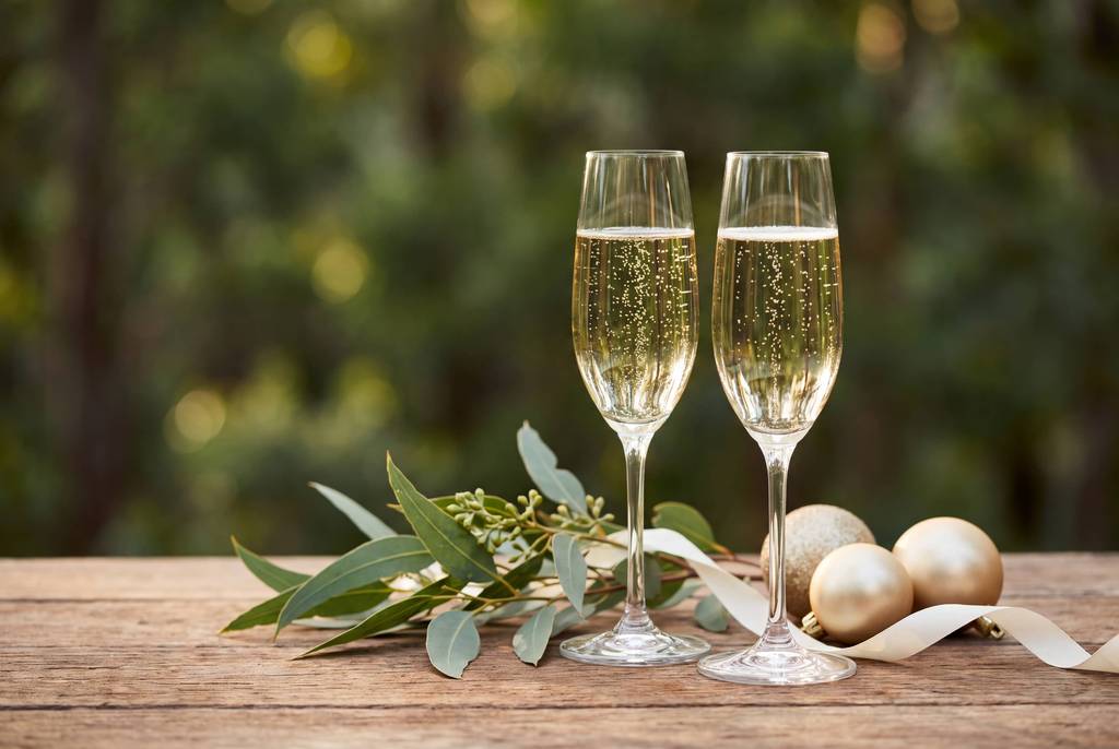 Two sparkling wine glasses beside gold baubles and eucalyptus on a timber table