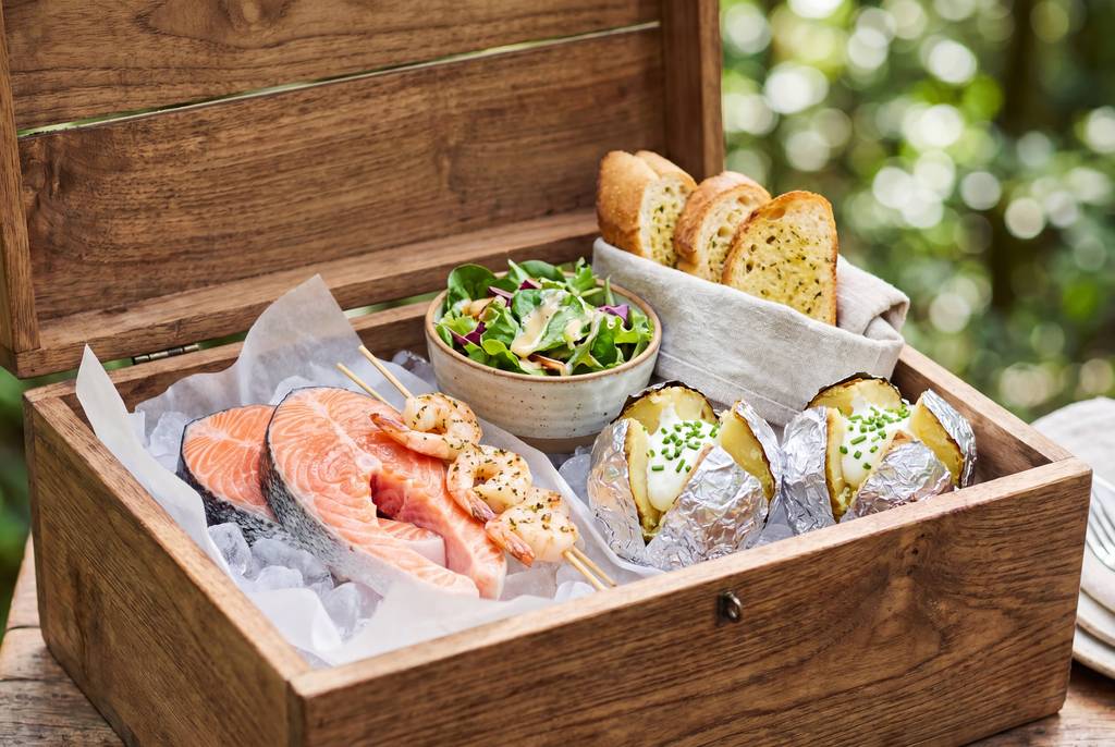 Timber hamper containing salmon fillet, green salad, herb bread and potatoes